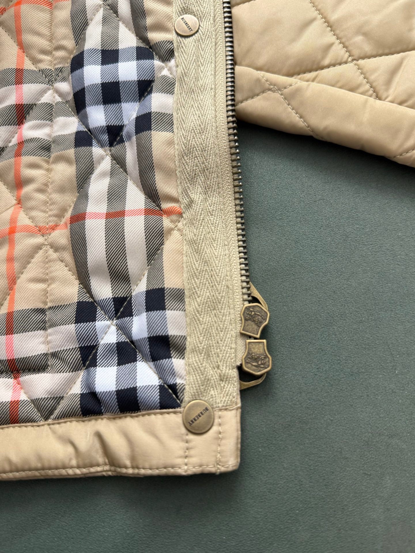 Quilted jacket hem with plaid lining edge and zipper pull hardware