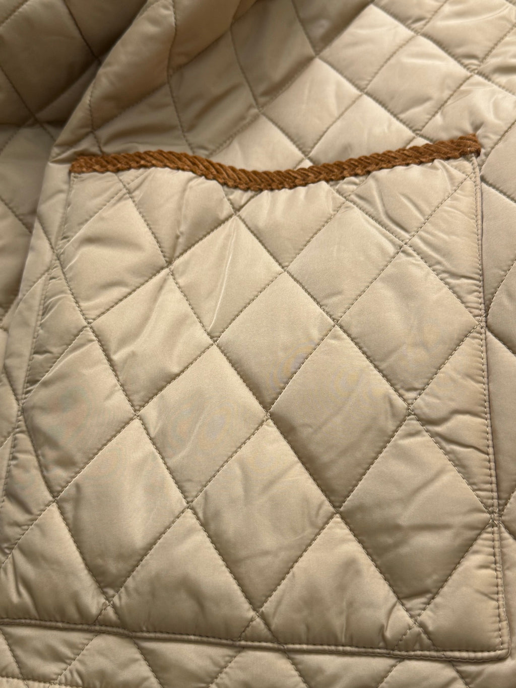 Quilted jacket front with diamond stitching and tan braided trim across the panel