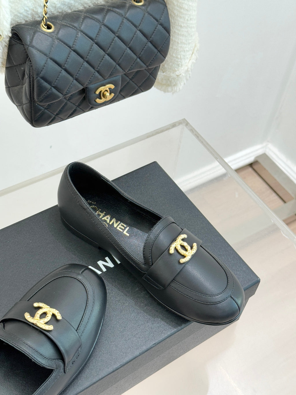 Chanel women’s black loafers with gold CC buckle detail, side view on box