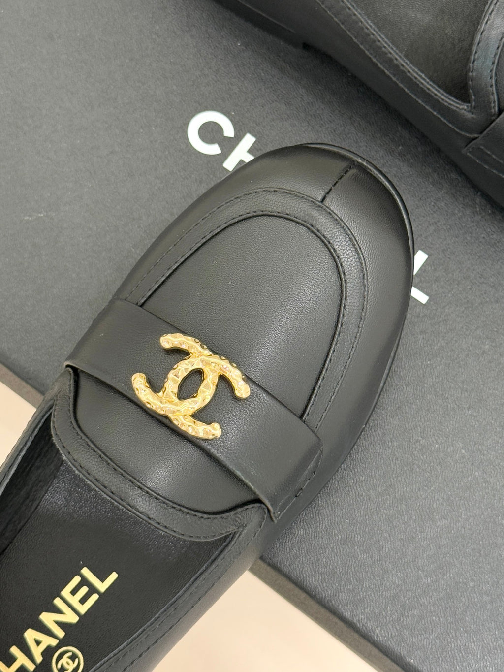 Chanel women’s black loafer close-up with gold CC emblem on front strap
