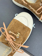Tan suede sneaker close-up with pink lace-up and chain logo ornament