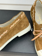 Tan suede sneaker with chain-like strap detail, pink laces, and white rubber sole