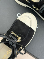 Black sneaker with gold chain detail, lace-up front, and off-white rubber sole