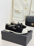 Black suede low-top sneakers with gold chain trim and white rubber sole