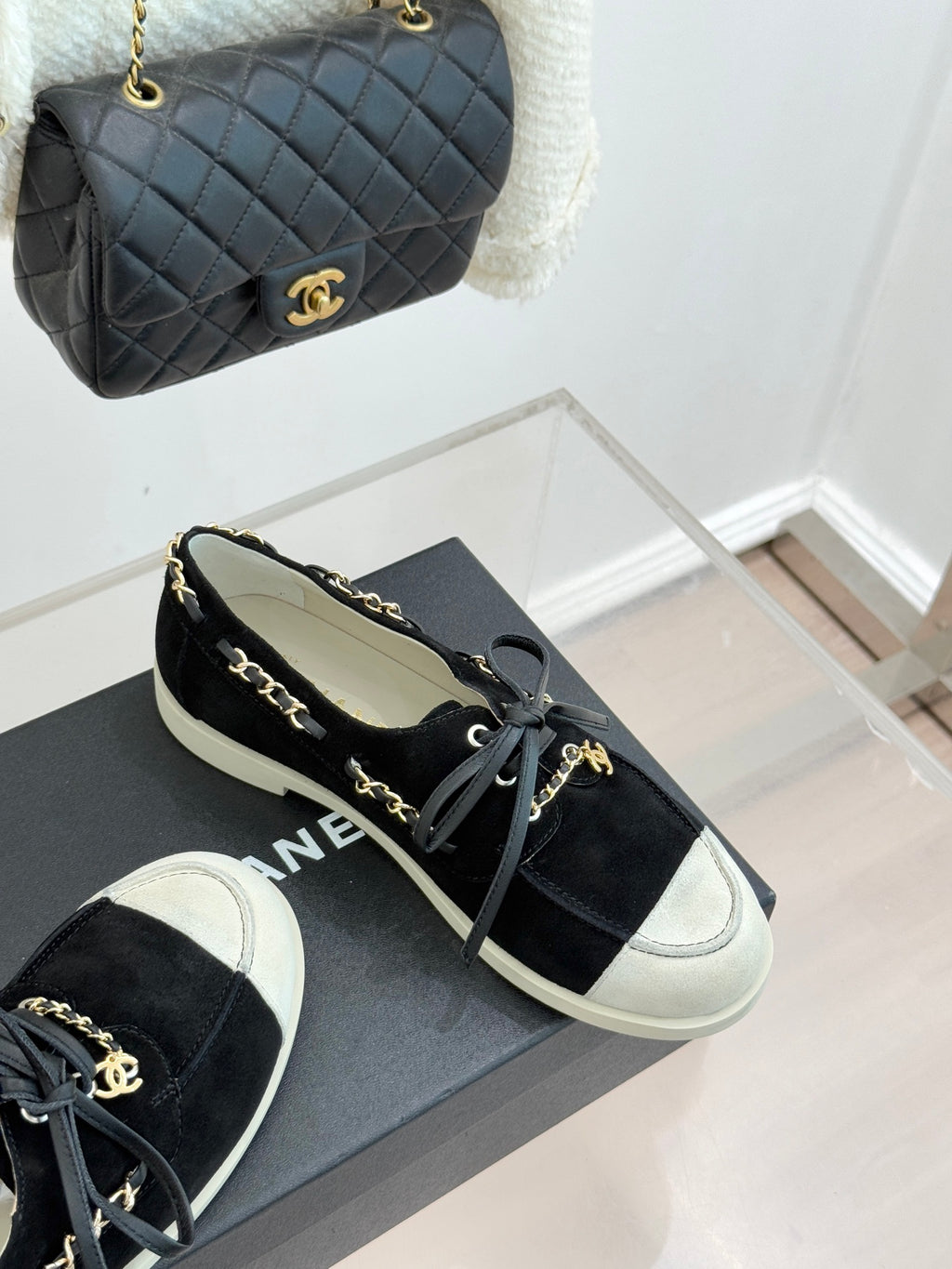 Black suede low-top sneakers with gold chain laces and white rubber sole