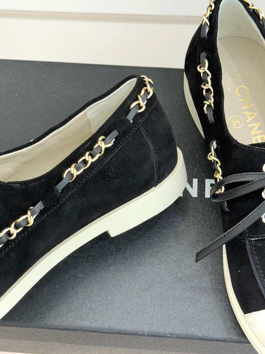 Close-up of black suede low-top sneakers with gold chain trim and white sole