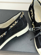 Close-up of black suede low-top sneakers with gold chain trim and white sole