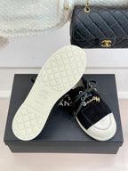 Black suede sneakers on a box, with white treaded outsole and gold chain trim