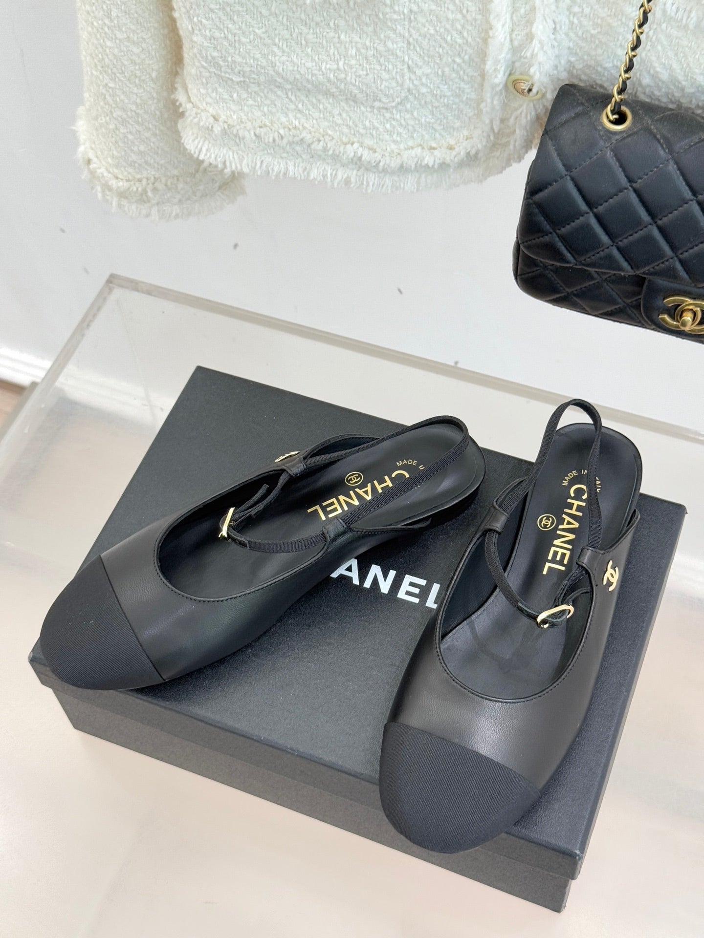 Dark slingback flats with gold buckle detail, pair on a shoe box