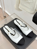 White Chanel flats with black side panels and gold-tone strap buckle on display box