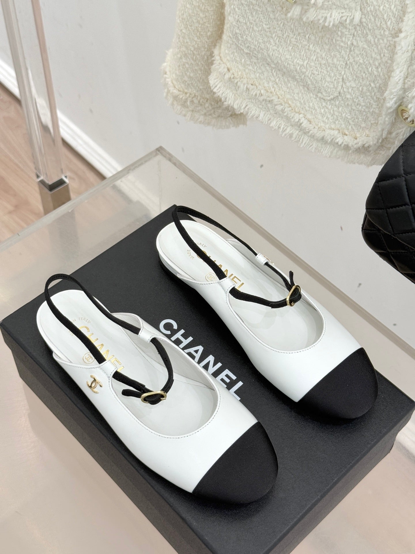 White Chanel flats with black side panels and gold-tone strap buckle on display box