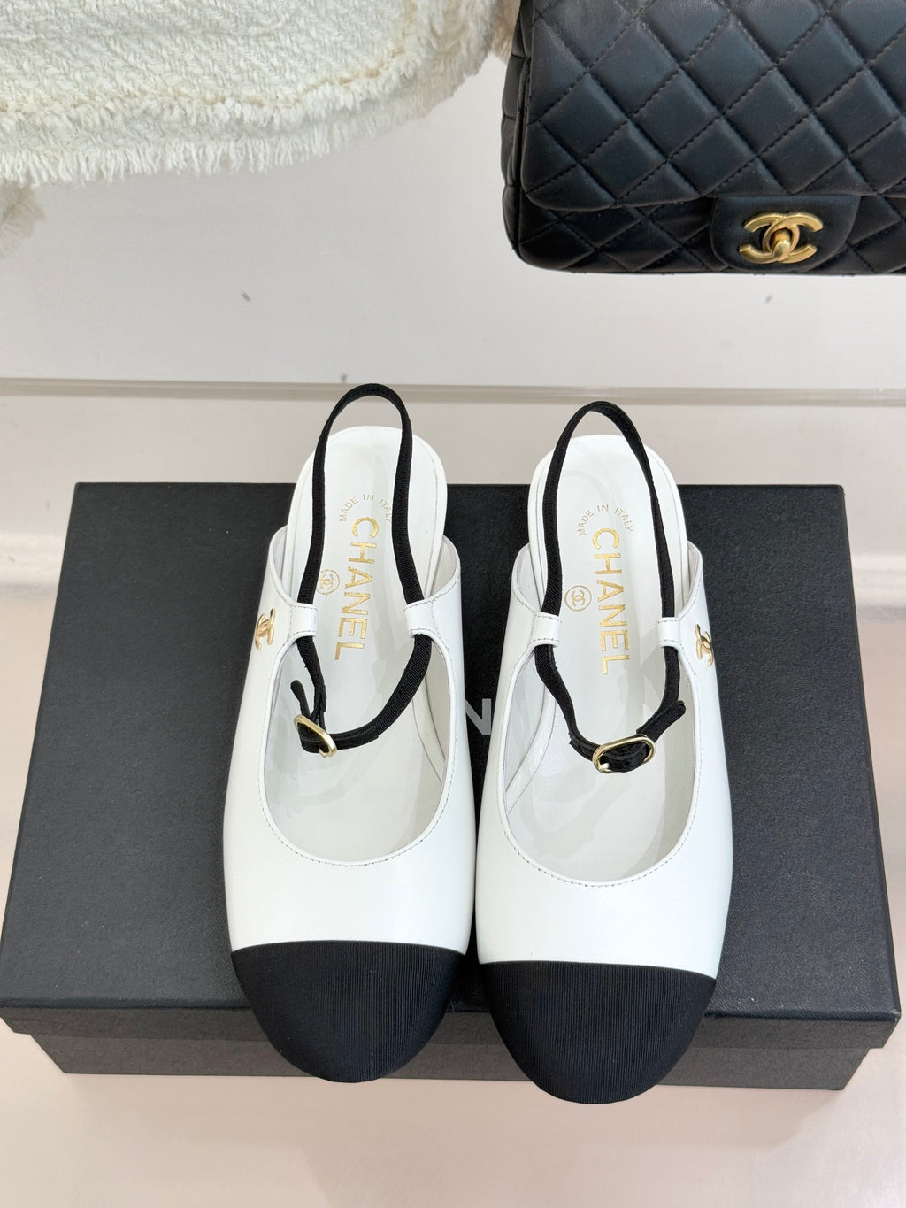 White Chanel flats with black trim, gold-tone strap buckle, and rounded toe