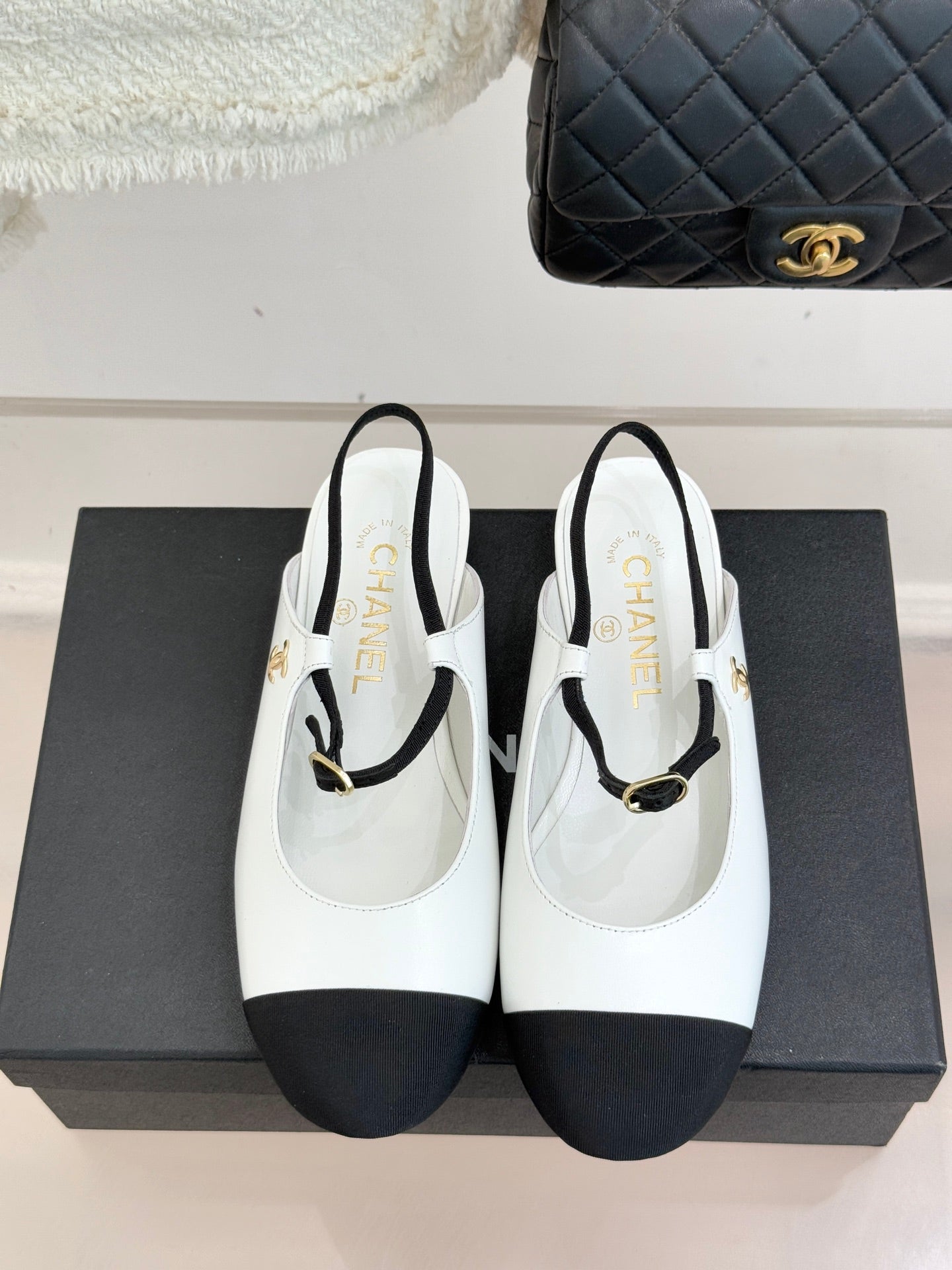White Chanel flats with black trim, gold-tone strap buckle, and rounded toe