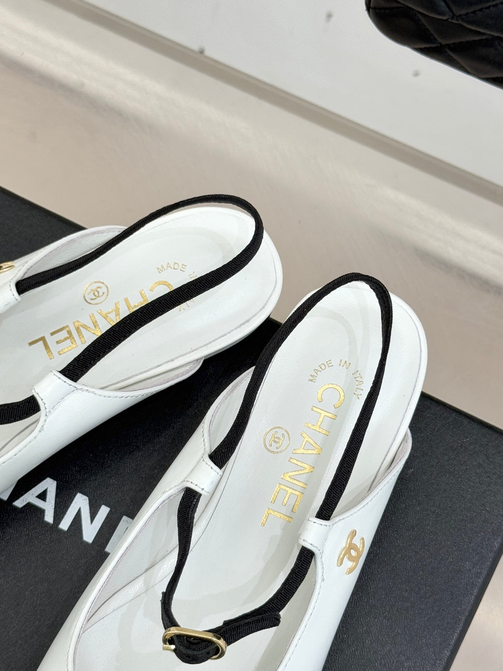 Chanel flats side view with white uppers, black trim, and gold buckle strap