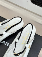 Chanel flats side view with white uppers, black trim, and gold buckle strap
