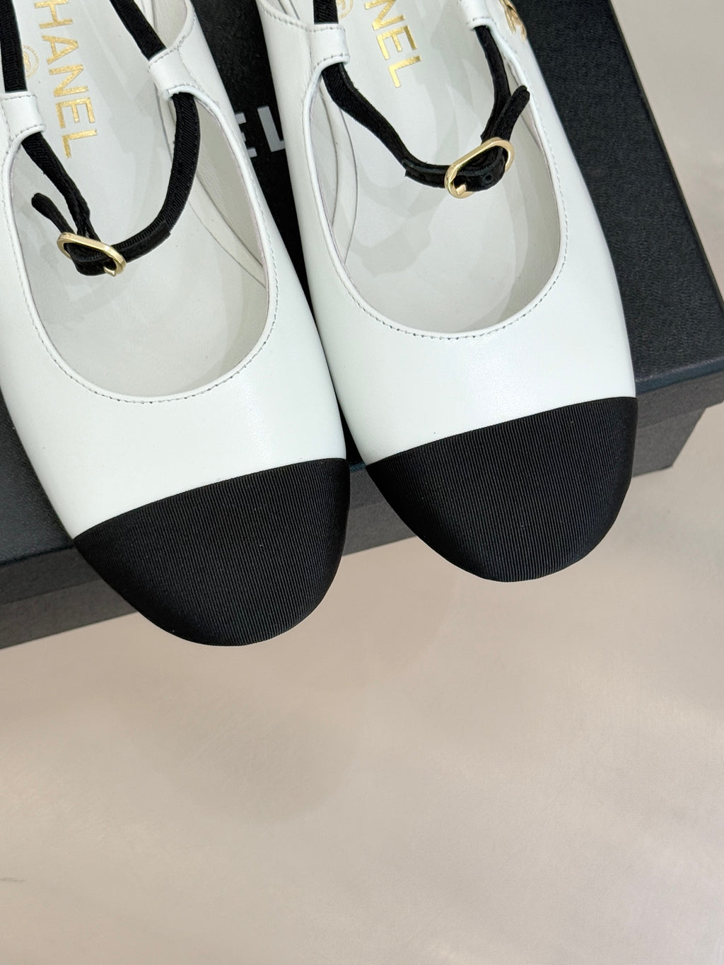 Close-up of white Chanel flats with black toe caps and gold-tone strap buckles