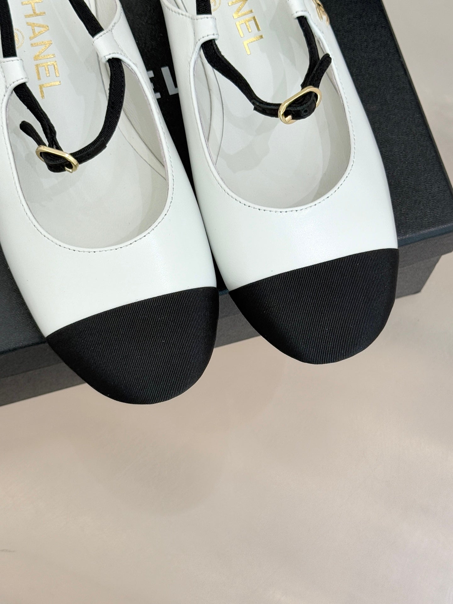 Close-up of white Chanel flats with black toe caps and gold-tone strap buckles