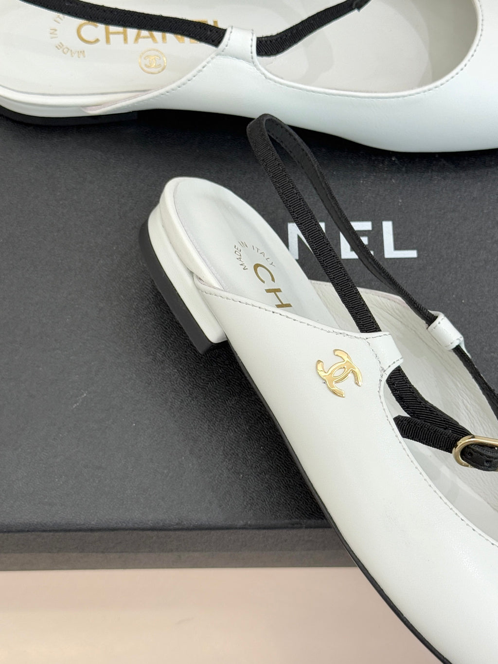 White Chanel flats close-up with gold emblem and black trim on toe