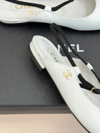 White Chanel flats close-up with gold emblem and black trim on toe