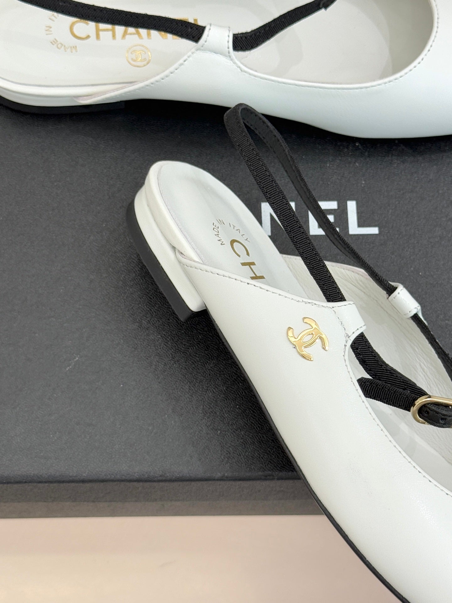 White Chanel flats close-up with gold emblem and black trim on toe