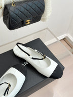 Chanel flats with white uppers, black toe panels, and gold-tone buckle strap
