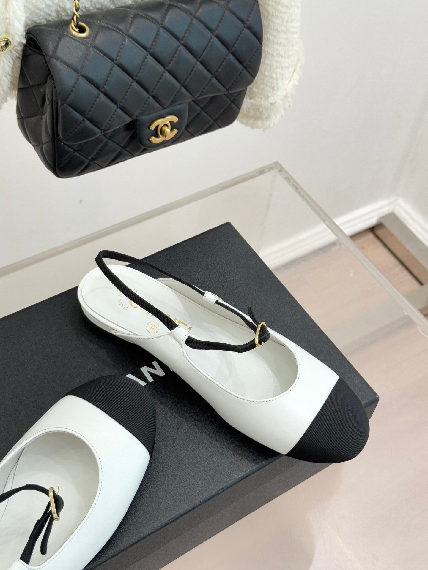 Chanel flats with white uppers, black toe panels, and gold-tone buckle strap