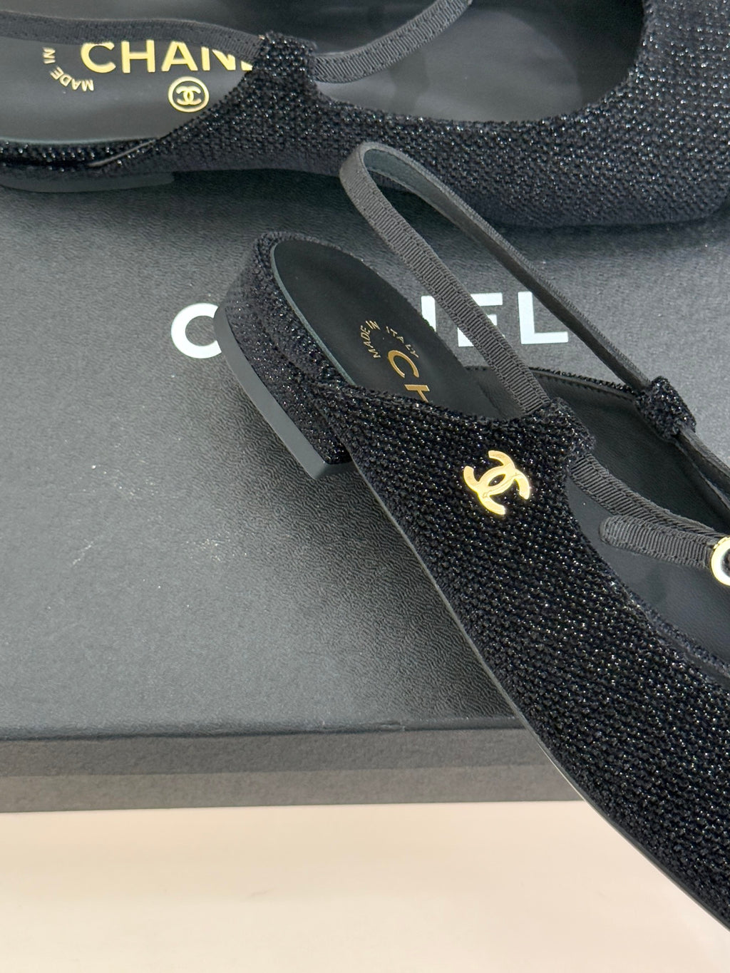 Chanel ladies black slingback flats close-up of gold CC charm on textured fabric