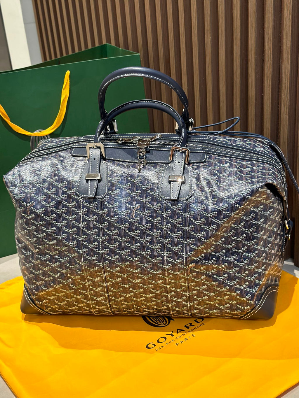 Goyard duffel bag front view, dark blue monogram canvas, top handles, metal zipper pull.