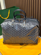 Goyard duffel bag front view, dark blue monogram canvas, top handles, metal zipper pull.