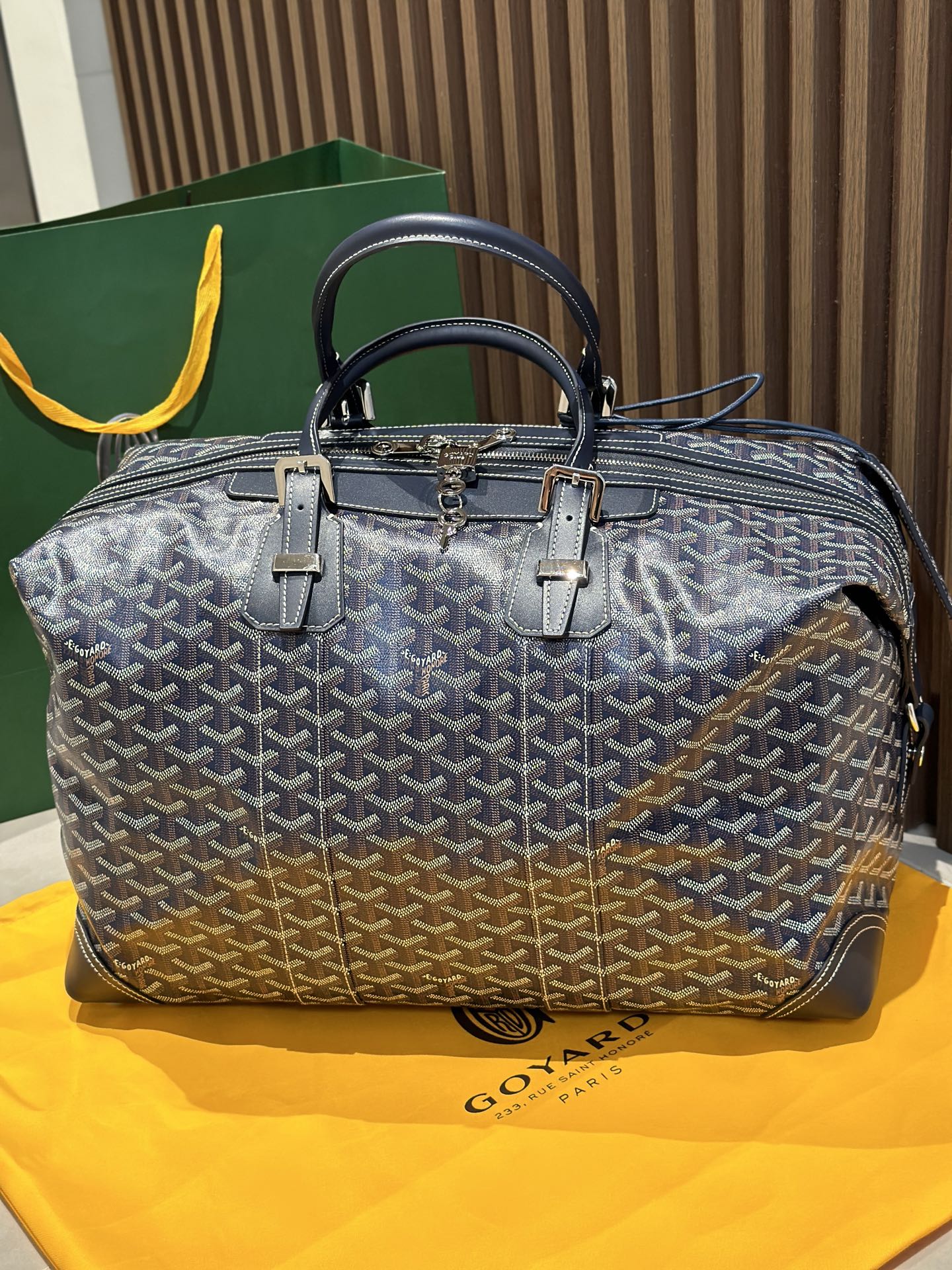 Goyard duffel bag front view, dark blue monogram canvas, top handles, metal zipper pull.