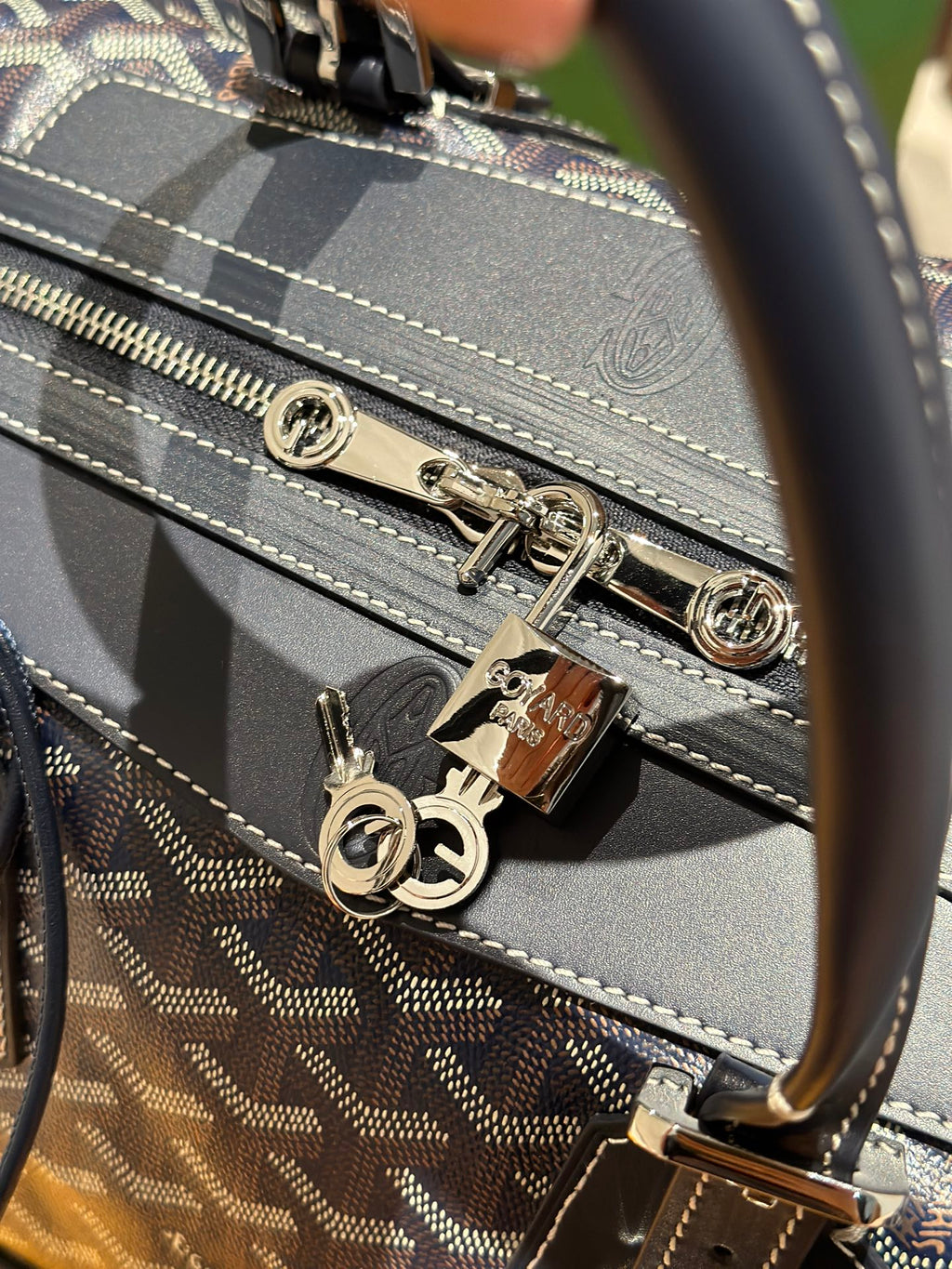 Goyard duffel bag zipper hardware with metal pulls on dark blue monogram canvas.