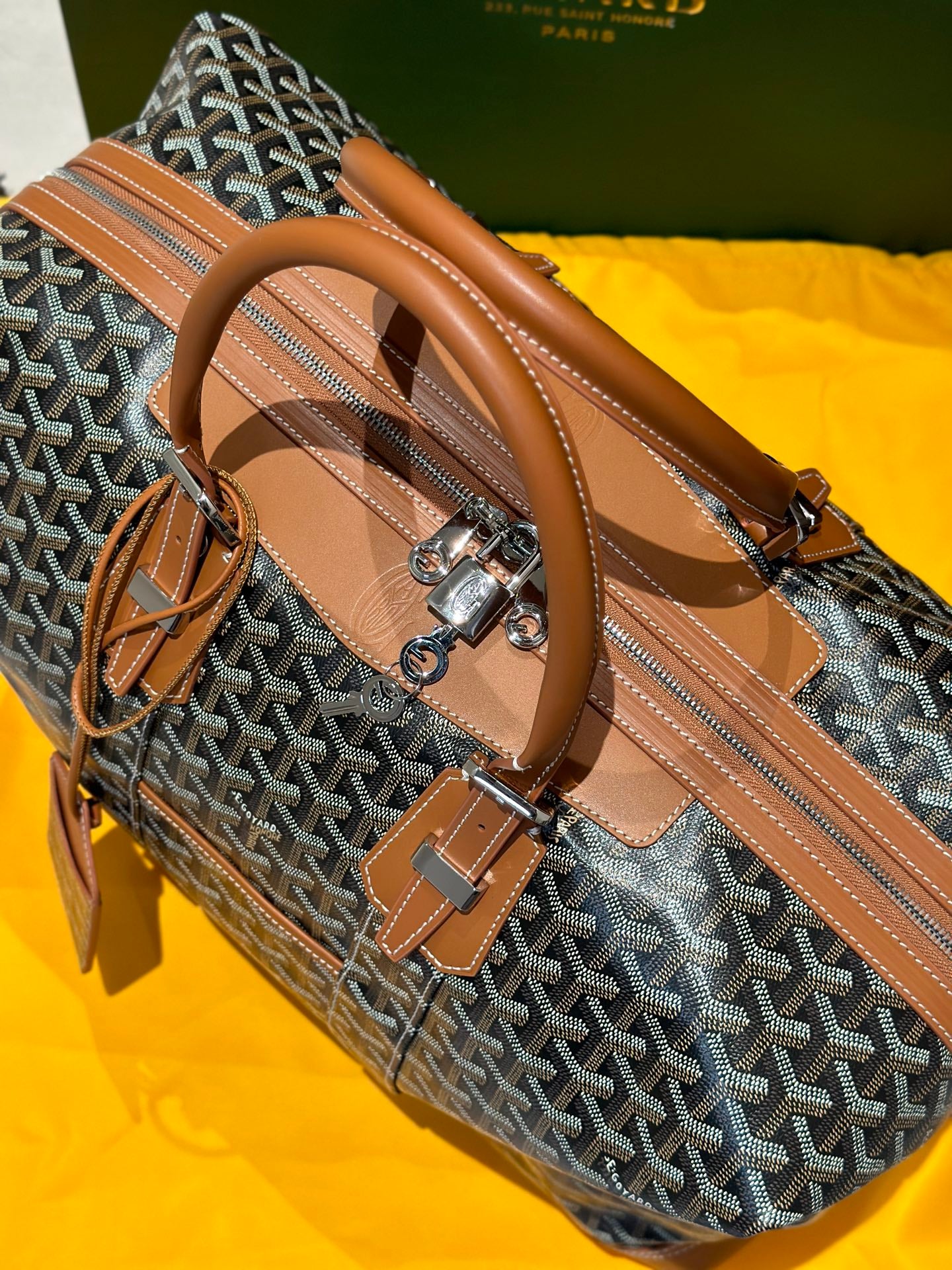 Goyard bag side view with tan leather trim, rolled handles, and silver zipper details