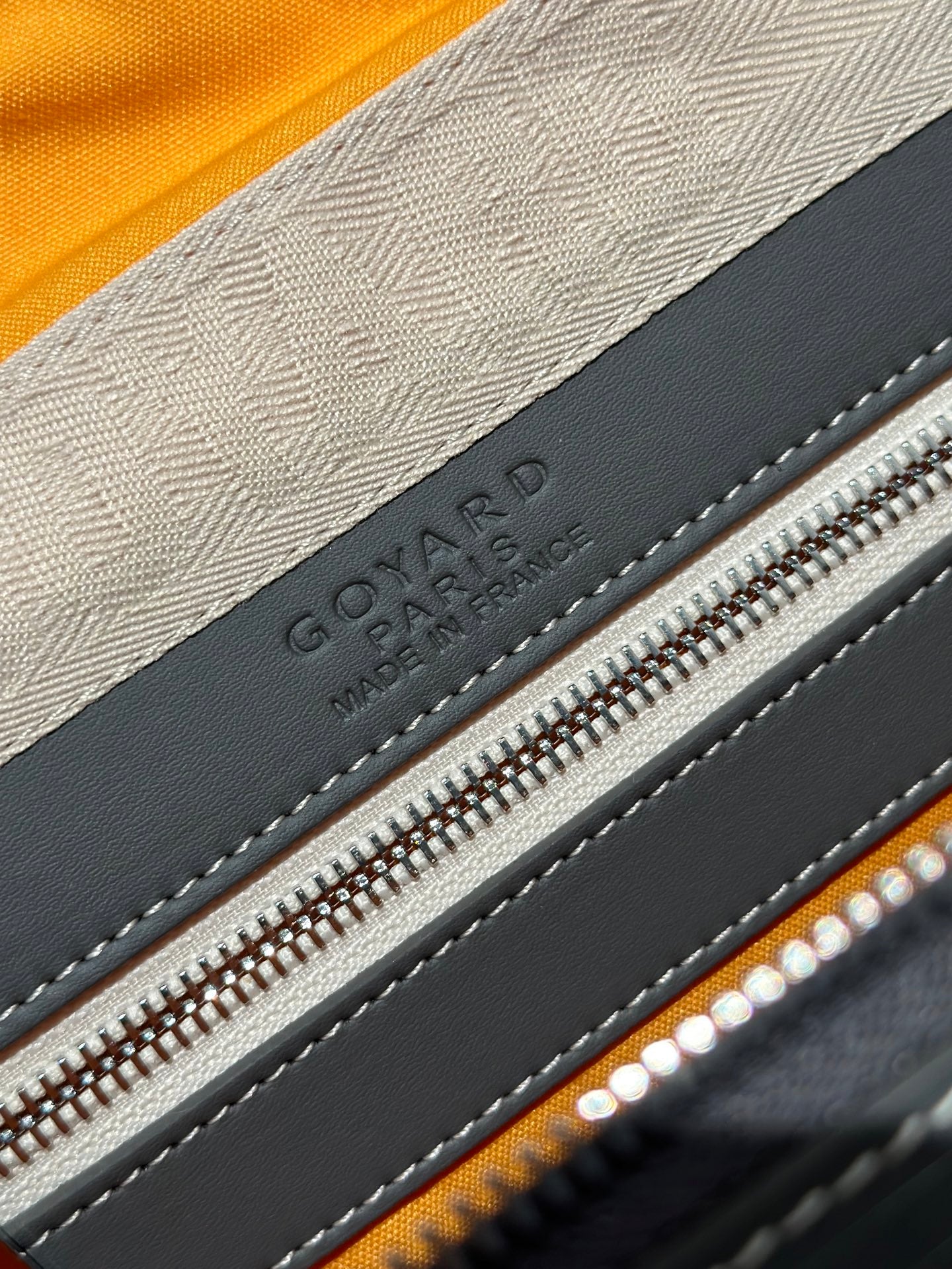 Goyard leather label detail with logo and silver zipper on dark gray trim