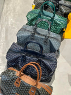 Goyard duffel bags in green, navy, and gray stacked with top handles and straps