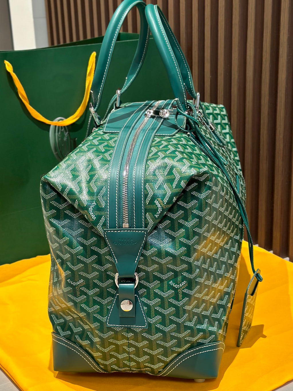 Green patterned duffel bag with top handles, front flap, and crossbody strap