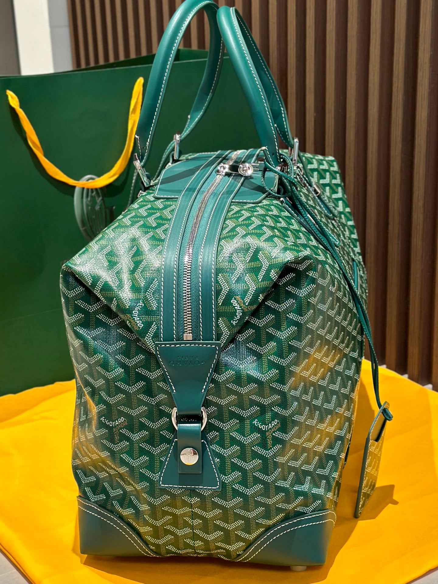 Green patterned duffel bag with top handles, front flap, and crossbody strap