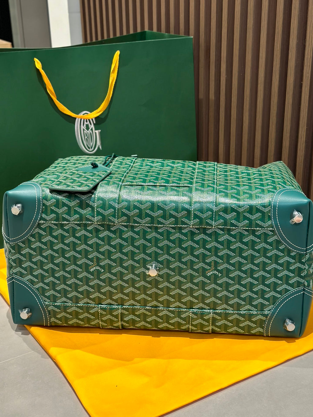 Green patterned duffel bag with front flap, studs, and top handles