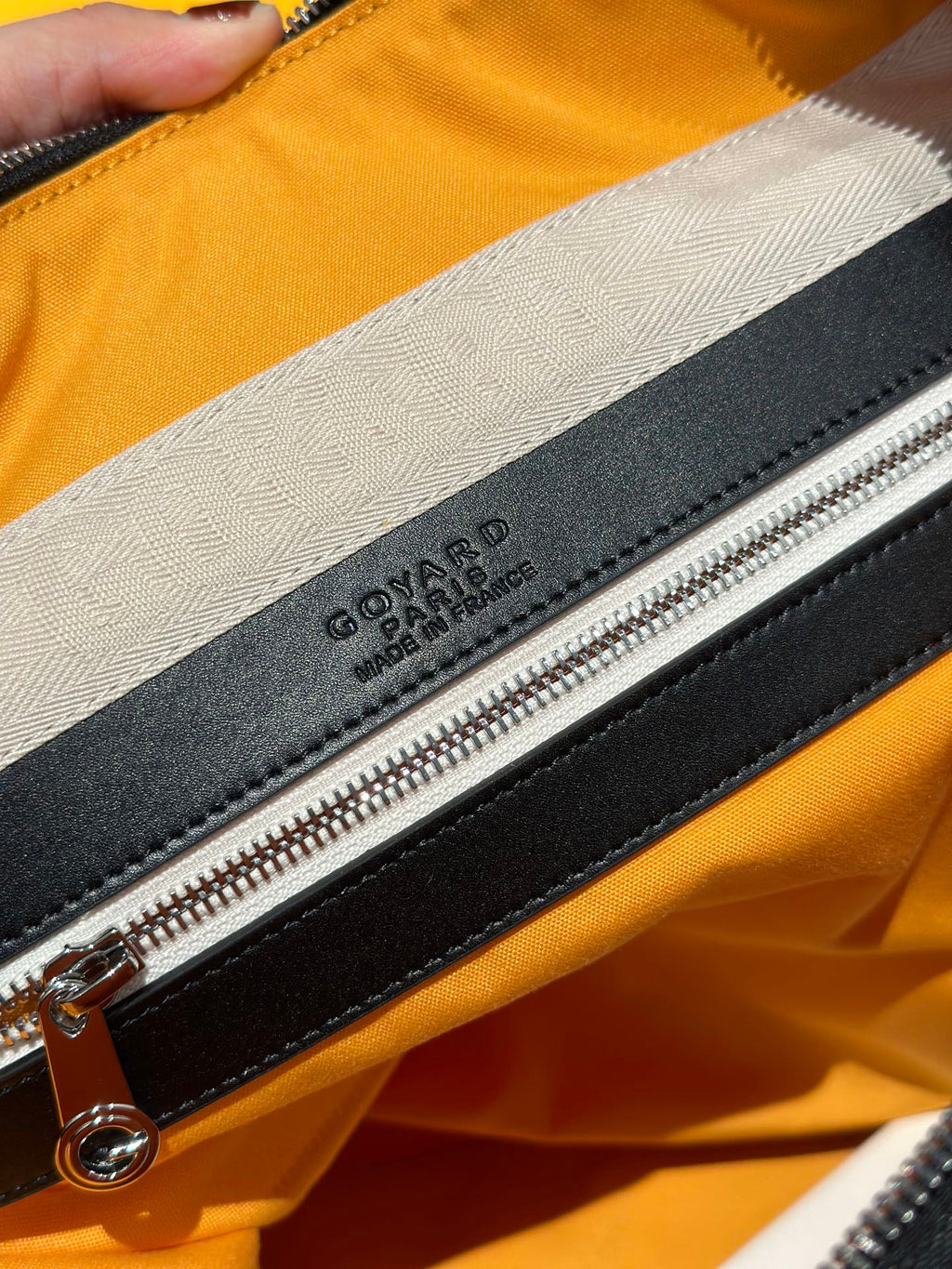 Goyard bag detail: black zipper with leather tab and embossed logo on lining