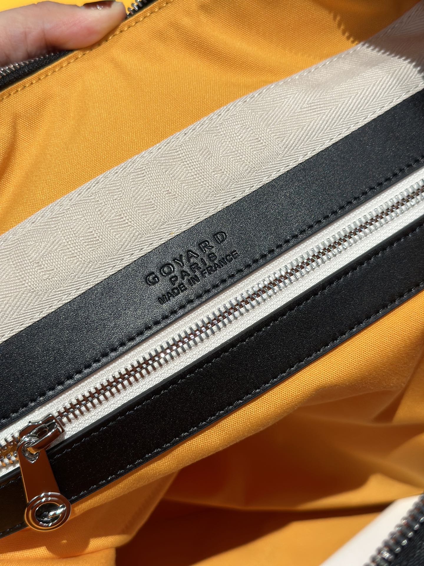 Goyard bag detail: black zipper with leather tab and embossed logo on lining