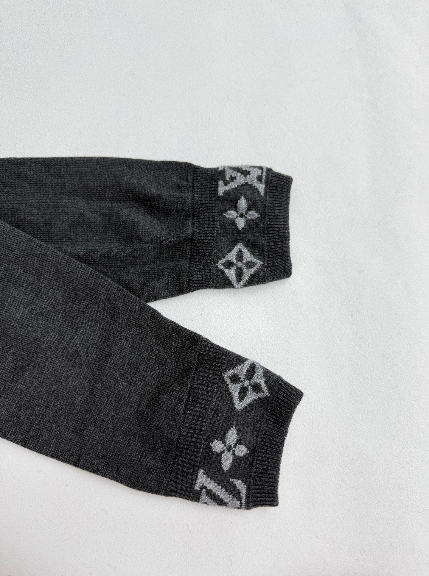 Dark gray sweater cuffs with patterned monogram details at sleeve ends