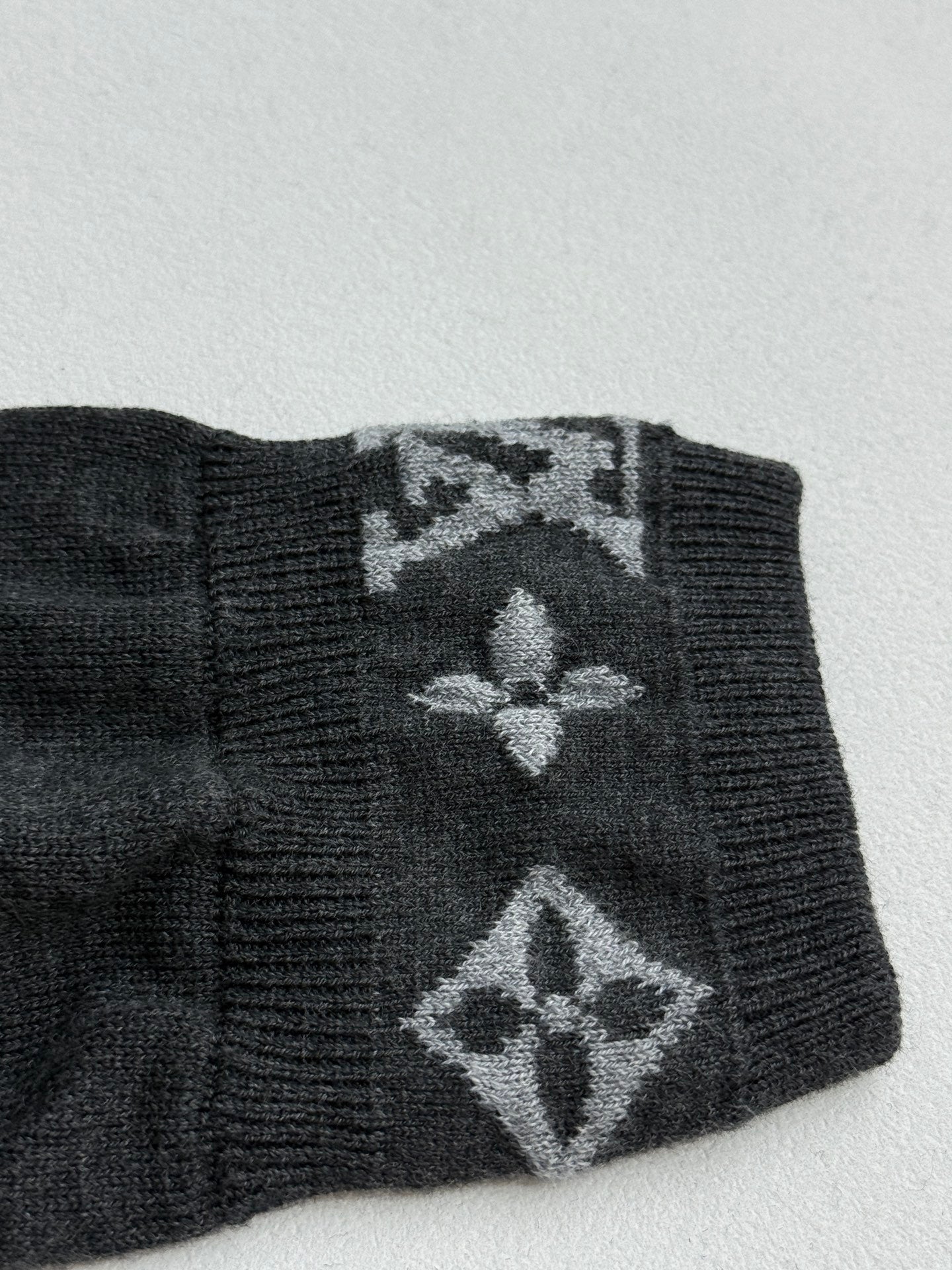 Dark gray sweater cuff with large monogram pattern and ribbed edge