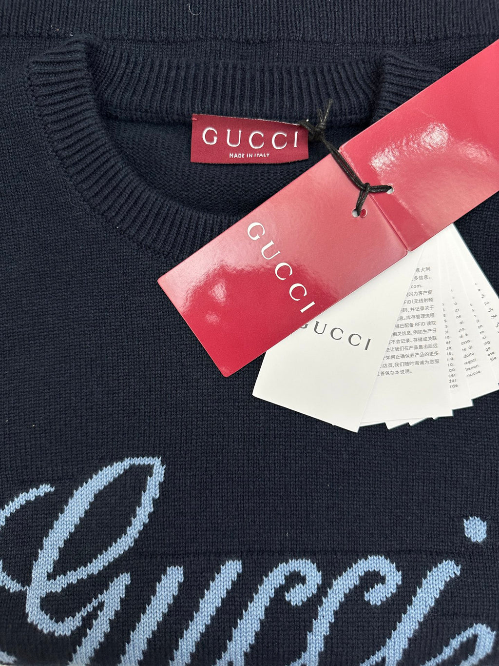 Navy knit sweater with red and white tags and partial 'Gucci' script
