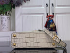Light beige croc-embossed handbag with structured flap, gold button details, and belt strap.