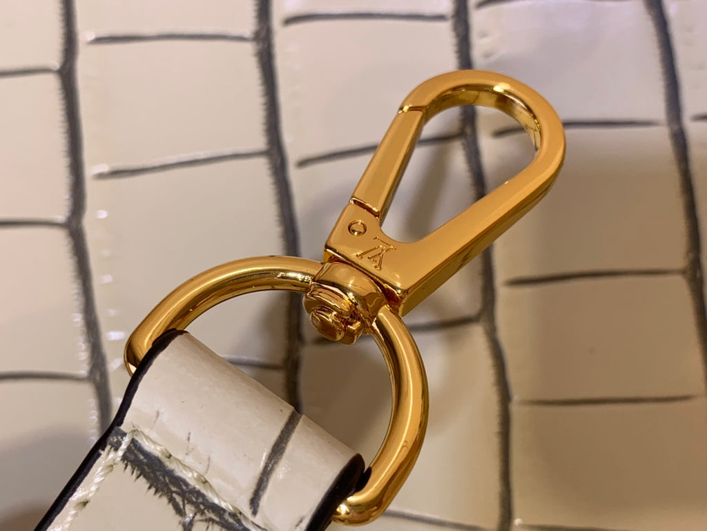 Gold swivel clasp hardware and D-ring attachment on a light beige croc-embossed strap.