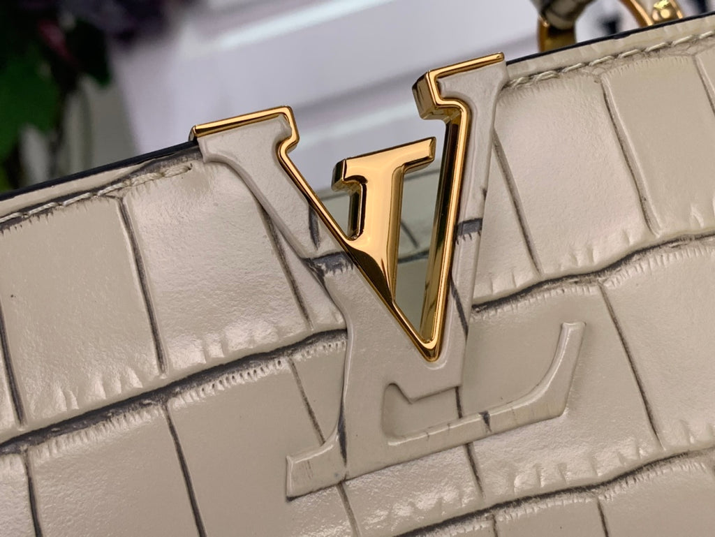 Close-up of Louis Vuitton gold LV logo on light beige croc-embossed flap.