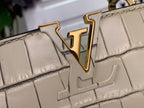 Close-up of Louis Vuitton gold LV logo on light beige croc-embossed flap.