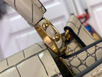 Close-up of gold clasp and croc-embossed strap attachment on a light beige handbag.