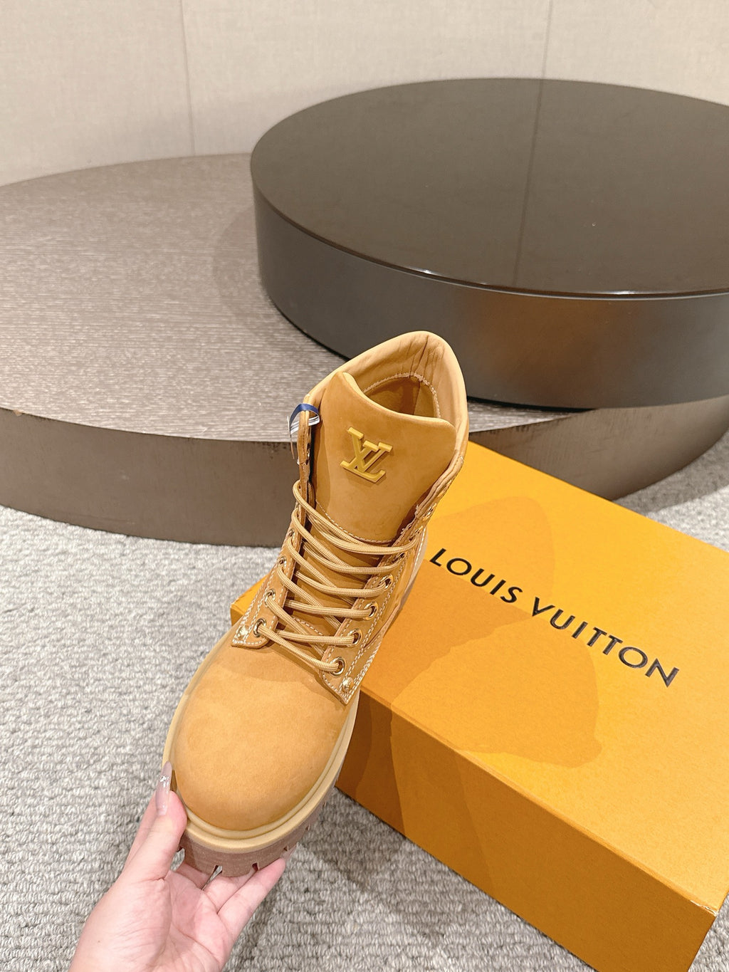 Tan lace-up ankle boot held in hand, showing inner lining and LV logo on side