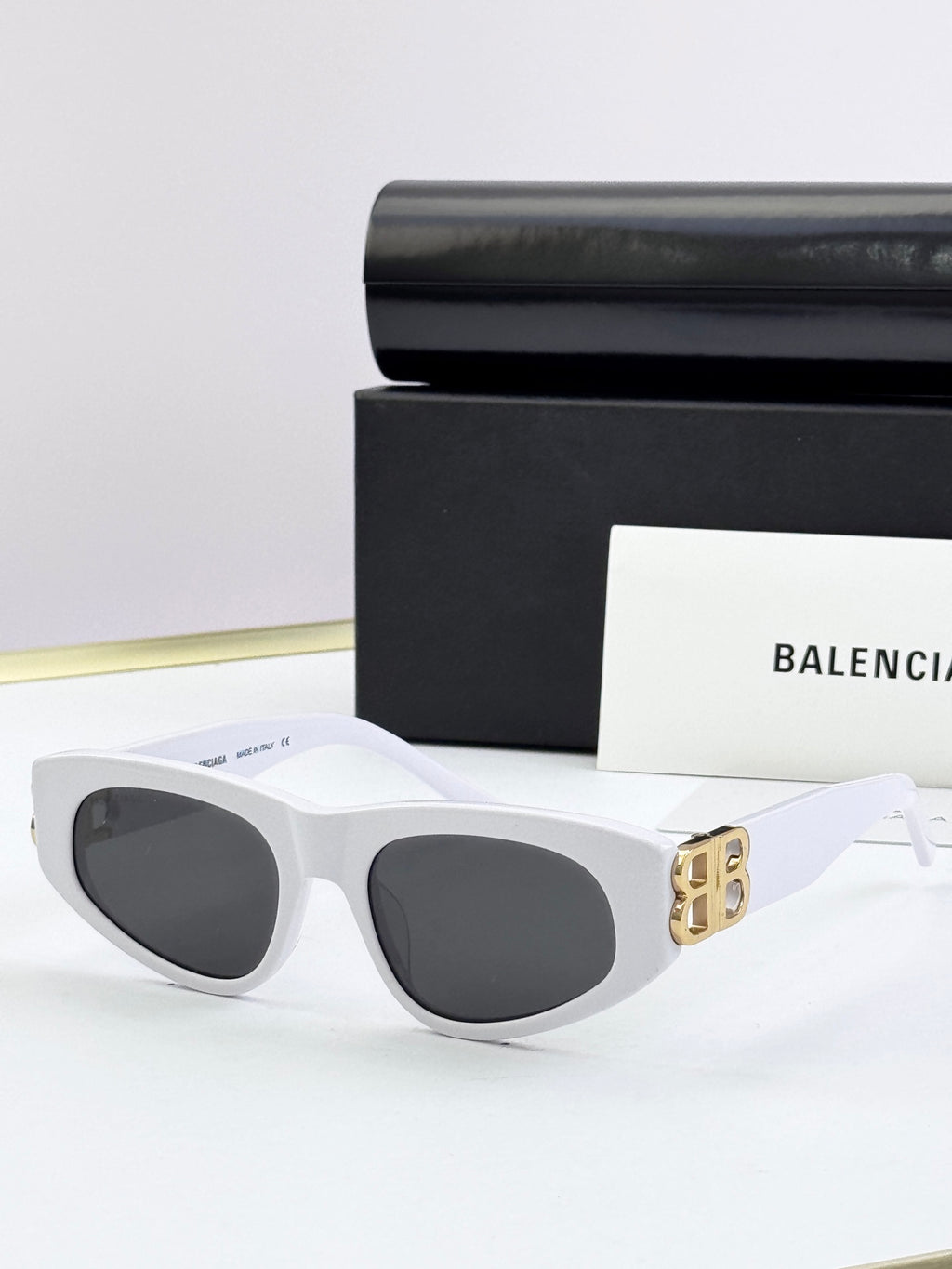 White cat-eye sunglasses with dark lenses and gold B logo on temples