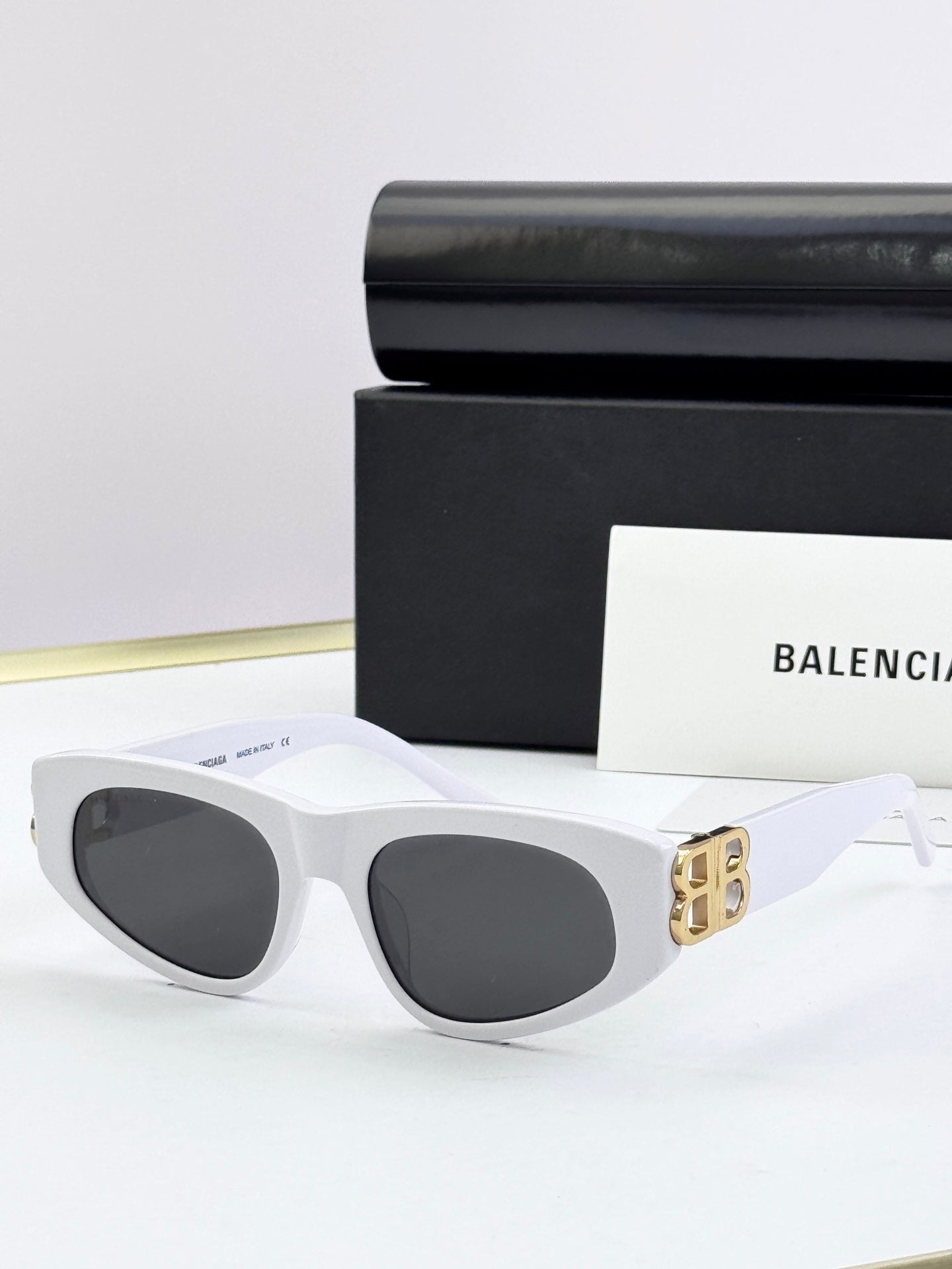 White cat-eye sunglasses with dark lenses and gold B logo on temples